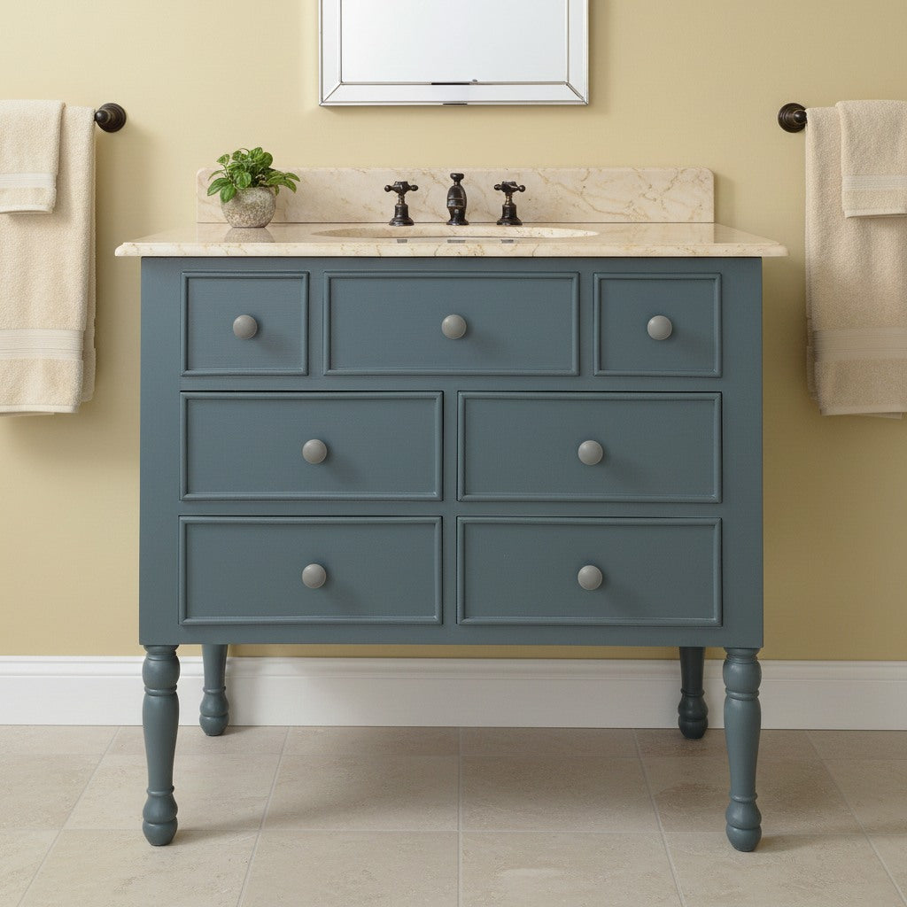 Blue bathroom vanity with marble countertop and beige towels on a yellow wall.
