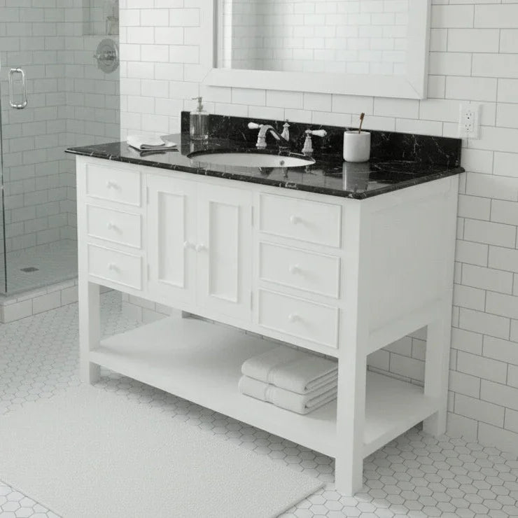 Bathroom vanity with black countertop and white cabinets in a tiled bathroom.
