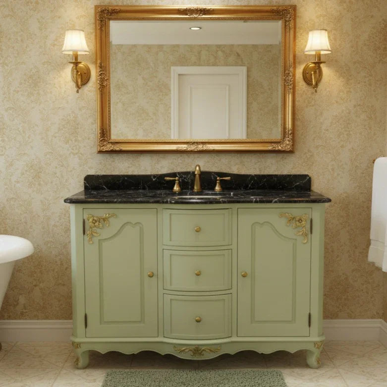 Bathroom vanity with gold-framed mirror and wall lights, featuring a green cabinet and black countertop.