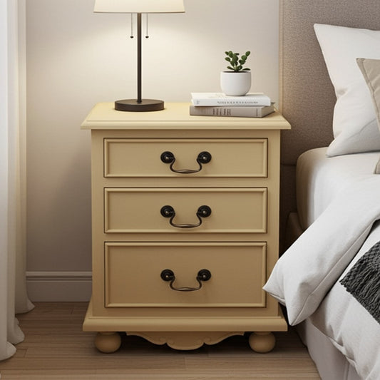 Beige nightstand with three drawers next to a bed in a bedroom setting.