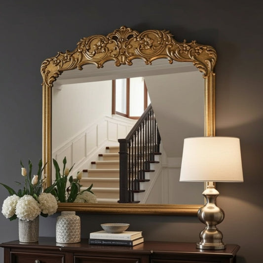 Decorative mirror with ornate frame on a wall above a wooden console table with a lamp and floral arrangement.
