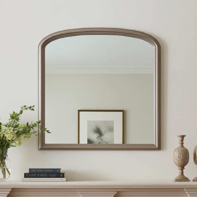 Wooden mirror on a wall with books and a vase below