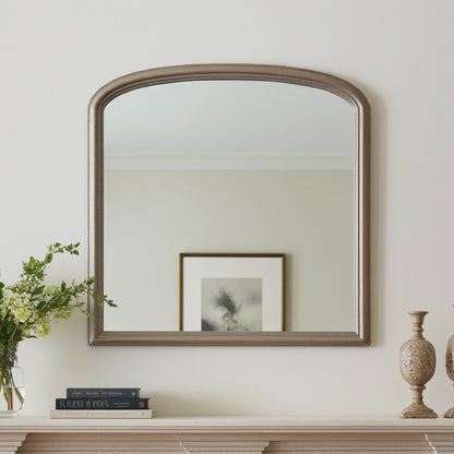 Wooden mirror on a wall with books and a vase below
