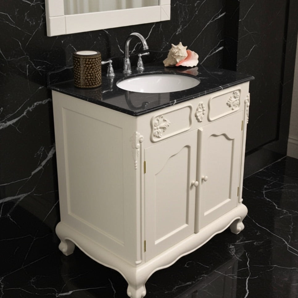Bathroom vanity with black countertop and white cabinet against a black marble wall.