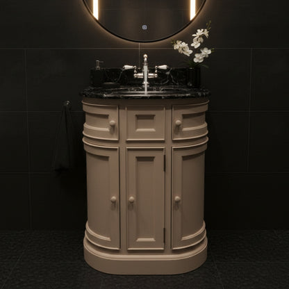 Beige bathroom vanity with black countertop and round mirror in a dark tiled room