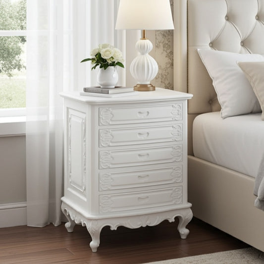 White nightstand with decorative lamp and flowers next to a bed in a bedroom.