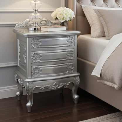 Silver nightstand with decorative elements next to a bed with beige bedding.
