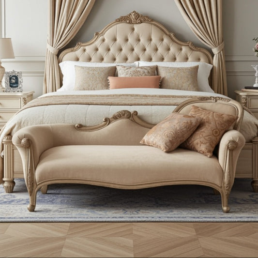 Beige upholstered bed with ornate headboard and chaise lounge in a bedroom setting.