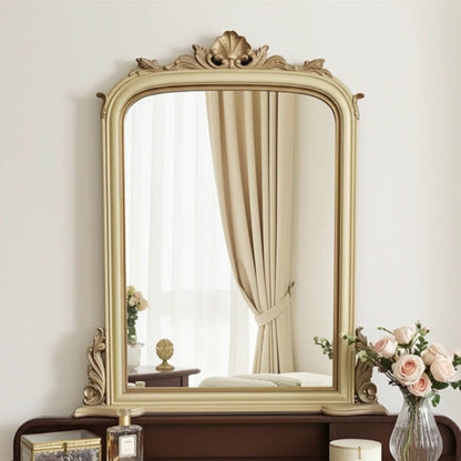 Decorative mirror with ornate frame on a wooden stand against a white wall.