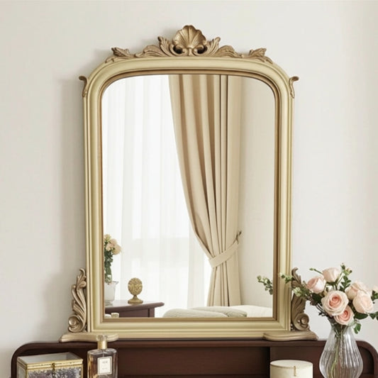 Decorative mirror with ornate frame on a wooden stand against a white wall.