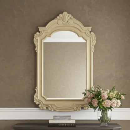 Decorative mirror with intricate frame on a wall with a vase of flowers on a table below.