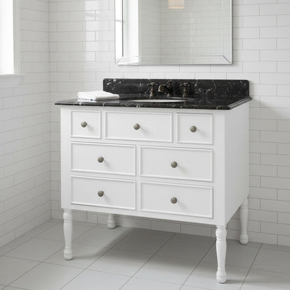 White bathroom vanity with black marble countertop against a tiled wall.