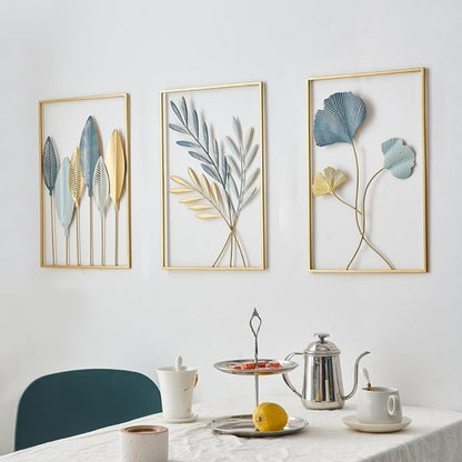 Three framed leaf art pieces on a wall above a dining table with a teapot and cups.