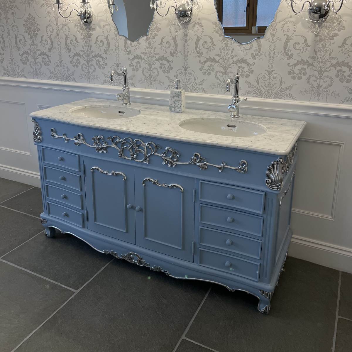 Blue bathroom vanity with marble countertop and ornate details in a bathroom setting.