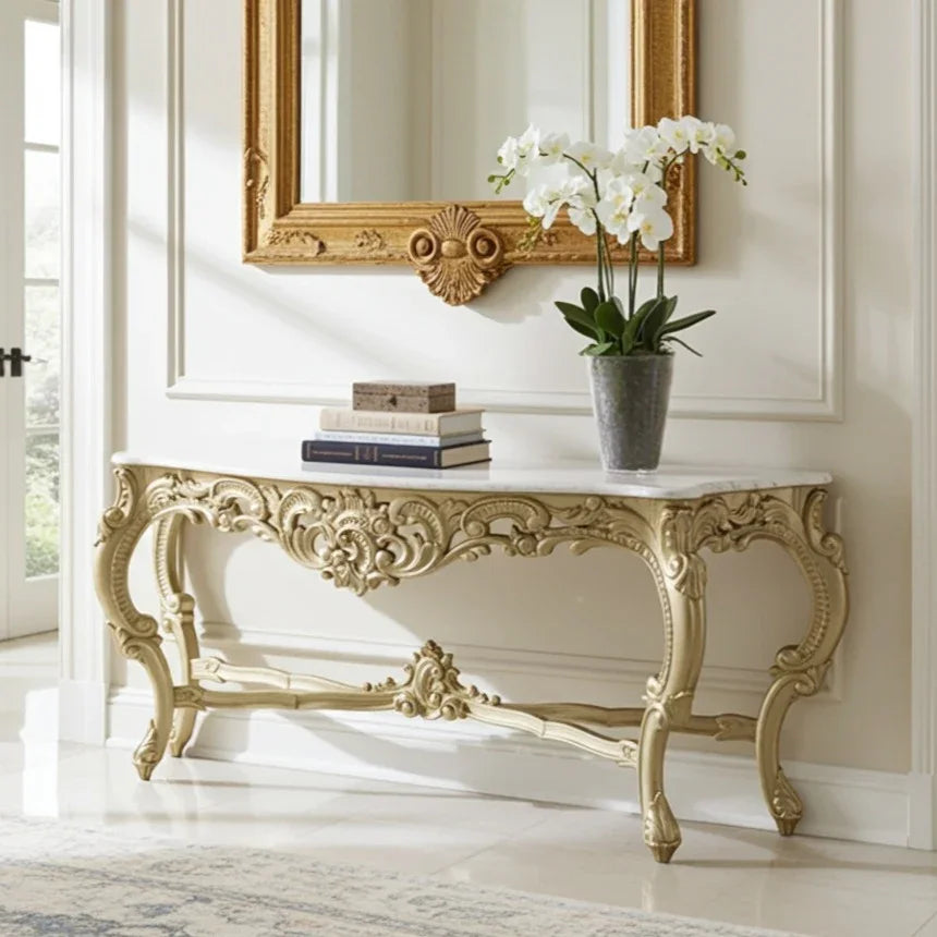 Decorative console table with ornate gold legs, white marble top, and a vase of white flowers in a room with a large mirror.