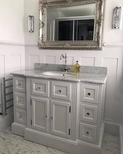 Bathroom vanity with marble countertop, sink, and decorative mirror.